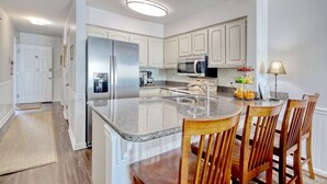 Una cocina moderna con armarios blancos, encimera de granito, electrodomésticos de acero inoxidable y sillas de madera.
