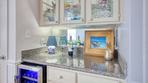 Una cocina con encimeras de granito, una copa de vino, un cuadro enmarcado y armarios de vidrio con objetos decorativos.