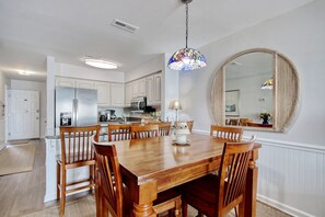 A dining area with a wooden table and chairs, a hanging light fixture, and a large mirror on the wall. - BEACHFRONT top-floor Condo next to Garden City pier with PRIVATE POOL! (Murrells Inlet)