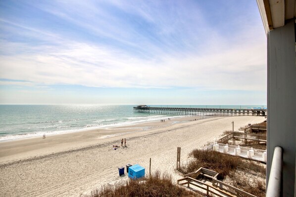 A beach with a pier extending into the ocean, sandy beach, and a view of the sea. - BEACHFRONT top-floor Condo next to Garden City pier with PRIVATE POOL! (Murrells Inlet)