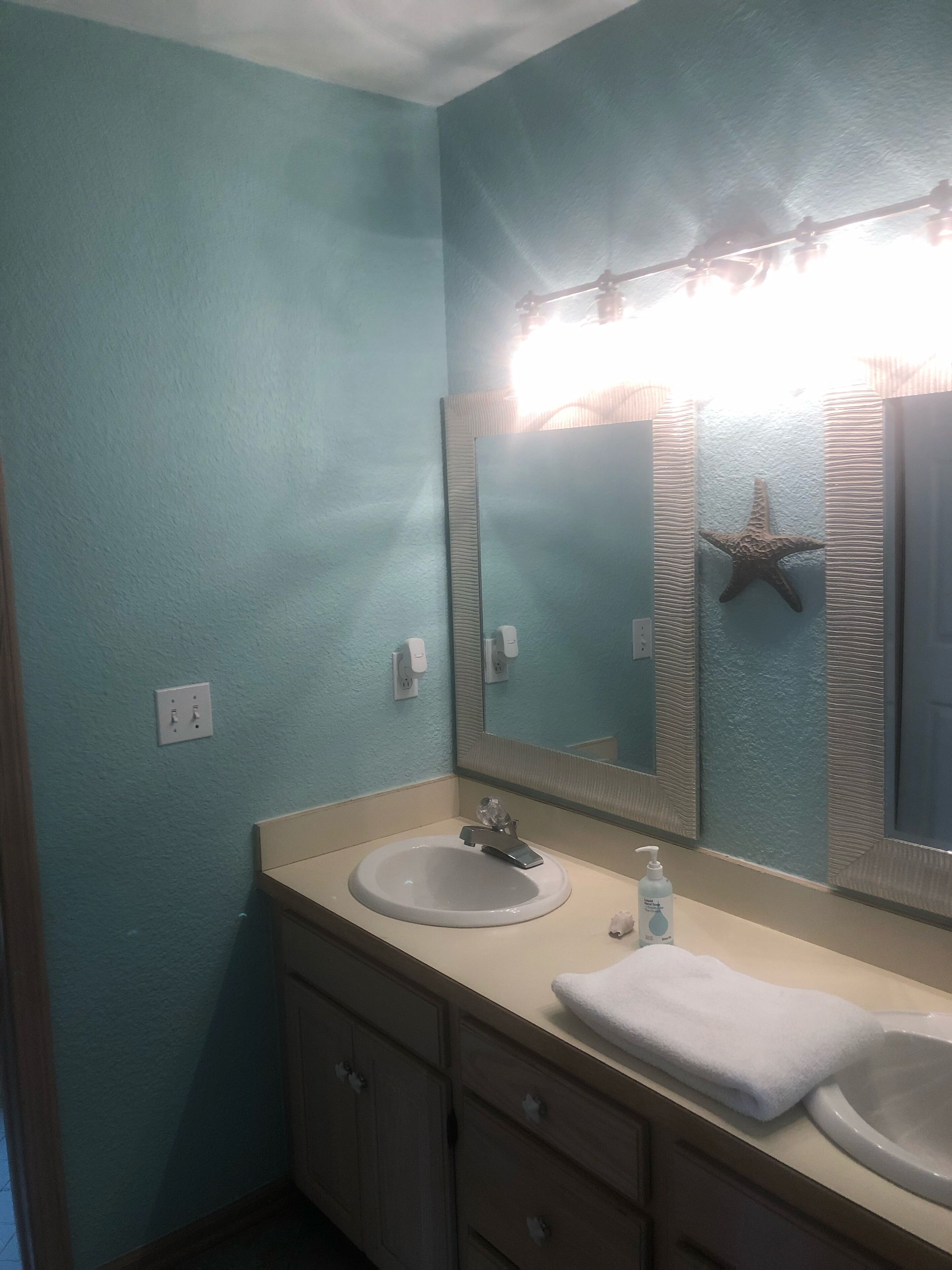A bathroom with a sink, mirror, starfish decoration, and a towel on the counter.