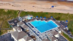An aerial view of a hotel with a large swimming pool, multiple guest rooms, and a beach area. - Two Crabby: Feels like home! Spectacular views, Beach Club Summer 2026! (Nags Head)
