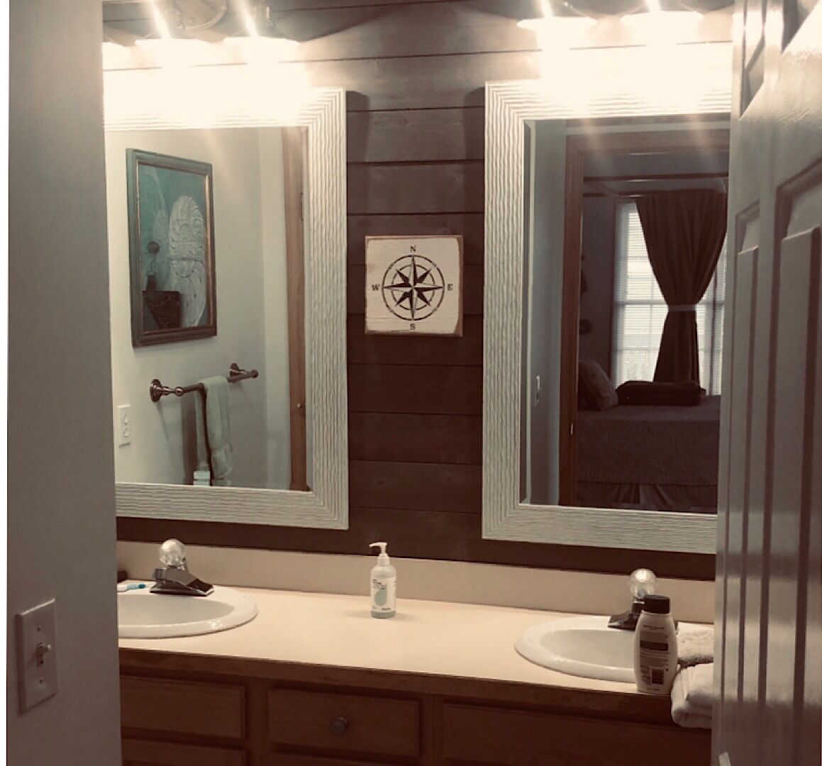 Un baño con dos lavamanos, un espejo, una decoración con brújula y una ventana con cortinas.