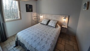 Une chambre avec un plafond en bois, un lit avec une literie à motifs, une fenêtre donnant sur des arbres et un luminaire fixé au mur.