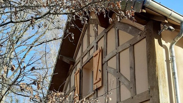 Un bâtiment traditionnel à colombages, doté de volets en bois, d’une fenêtre visible et d’une gouttière en métal.