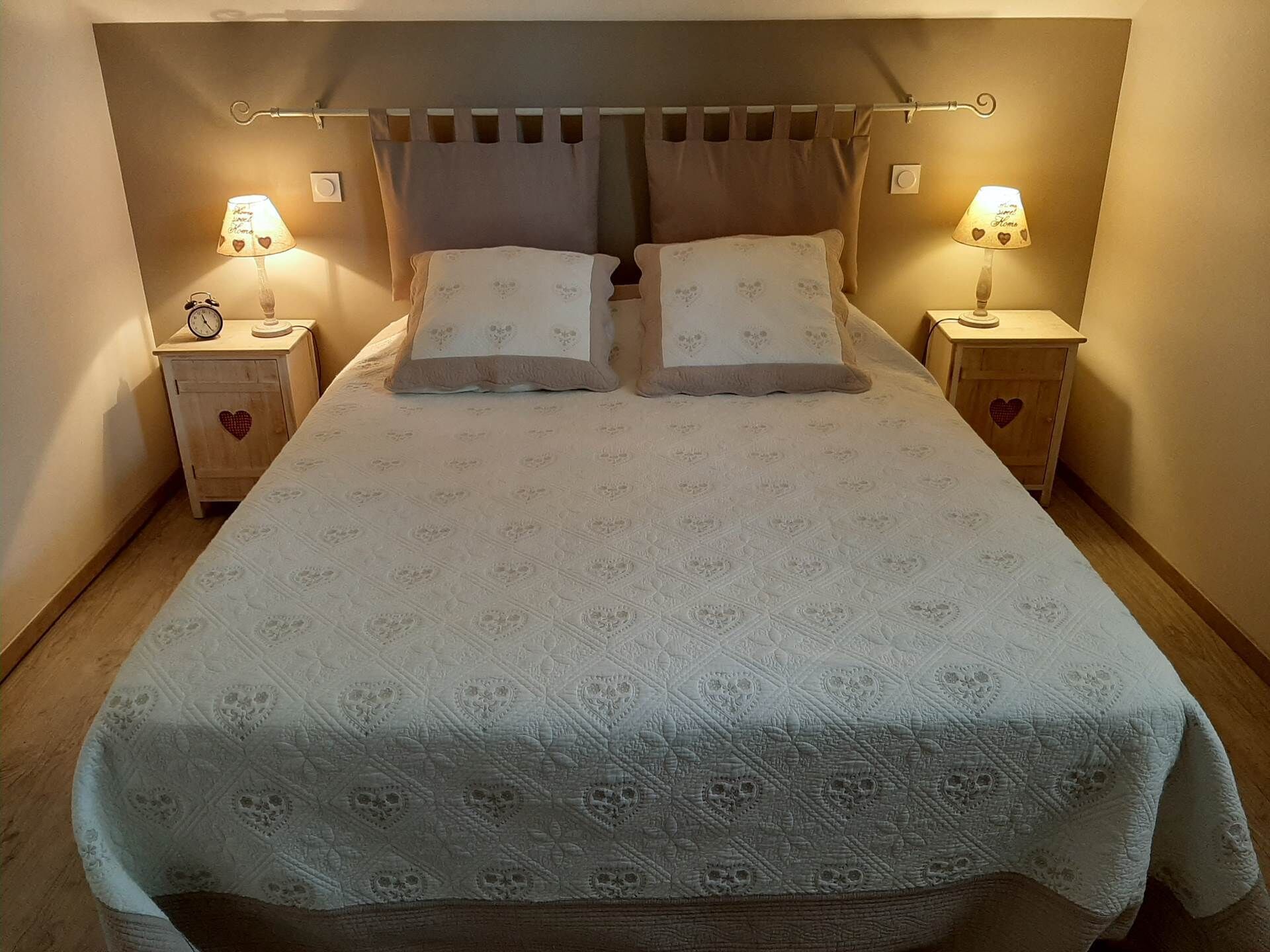 A neatly made bed with a patterned bedspread, two pillows, and two bedside tables with lamps and clocks.