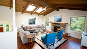 A spacious living room with a stone fireplace, wooden beams, and large windows. - Jack's Peak Retreat (Carmel)