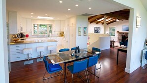 A spacious kitchen with white cabinets, a central island, and blue bar stools. - Jack's Peak Retreat (Carmel)