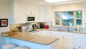 A modern kitchen with white cabinets, a large island with bar stools, a microwave, stove, and a coffee maker. - Jack's Peak Retreat (Carmel)