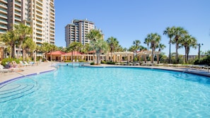A swimming pool with lounge chairs and palm trees, surrounded by high-rise buildings.