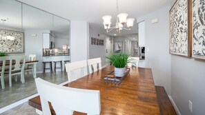 A dining area with a wooden table, white chairs, a chandelier, and a potted plant. - Golf Cart ~ Beach Front ~ Balcony ~ Community Pool (Miramar Beach)