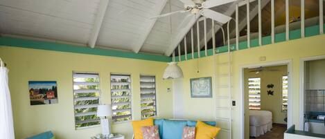 A spacious living area with a high ceiling, a ceiling fan, a sofa set, a coffee table, and a dining table with chairs.
