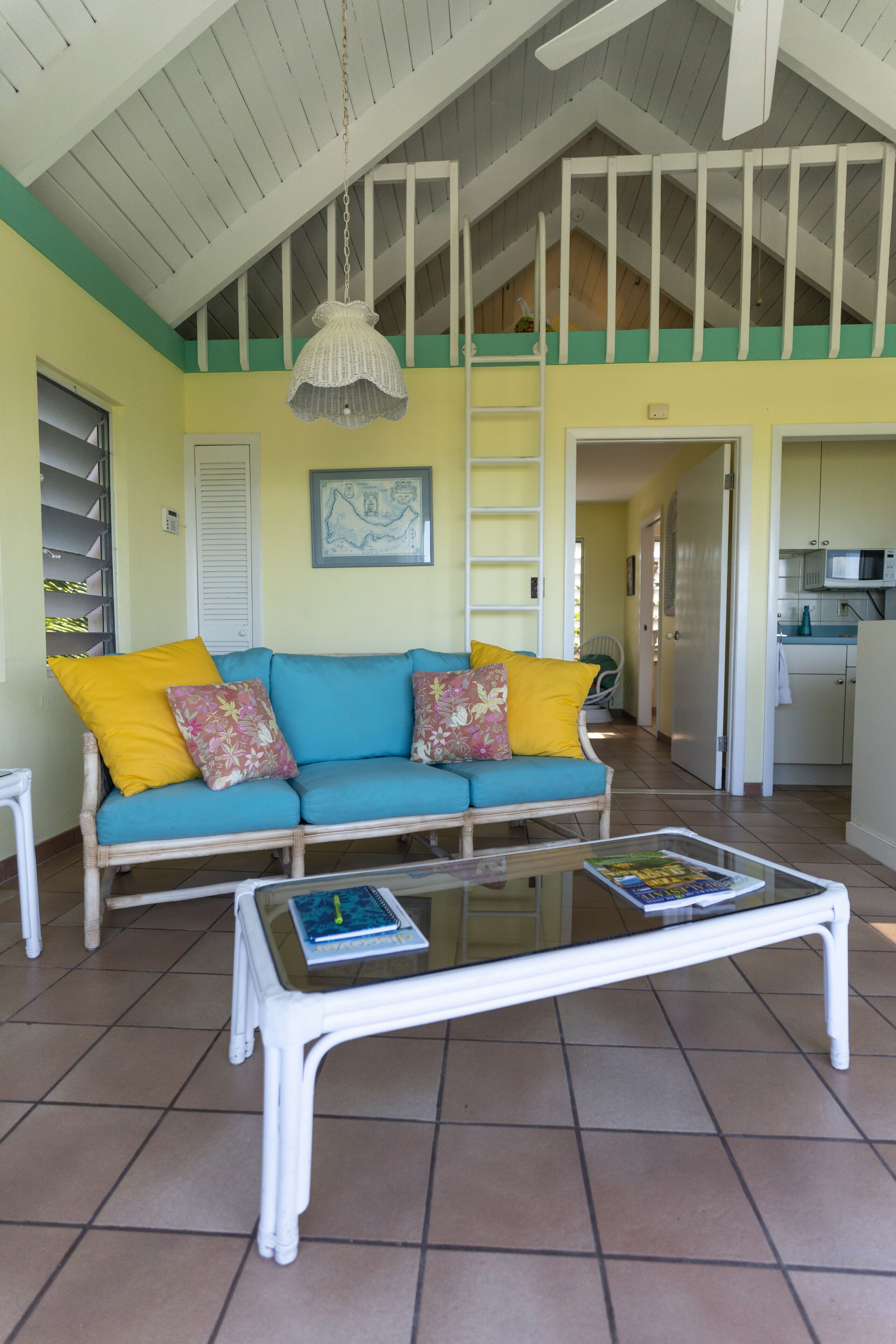 A living room with a blue sofa, yellow cushions, a glass coffee table, and a hanging light fixture.