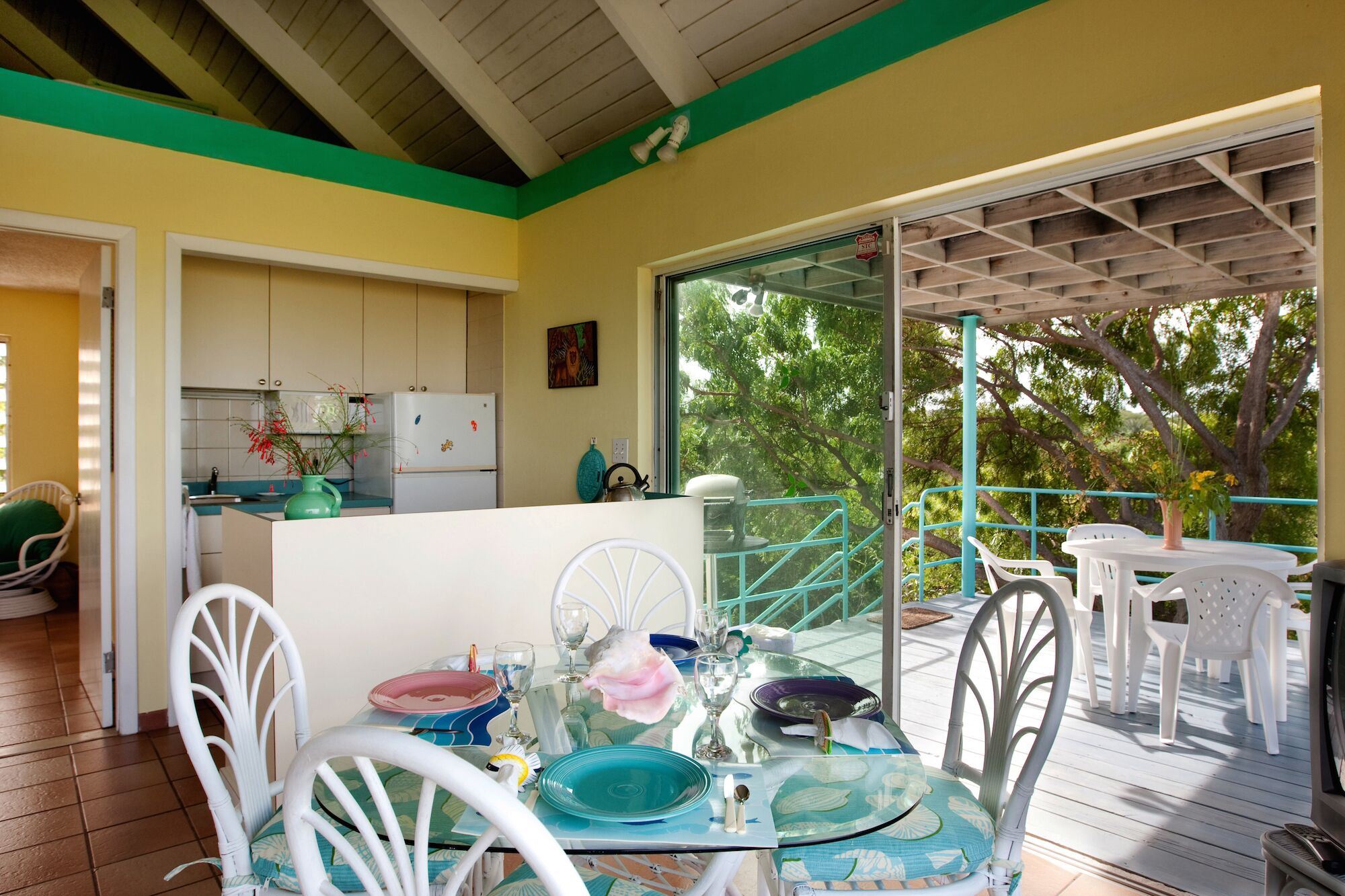 A dining area with a glass table, white chairs, and a view of a balcony with a railing.