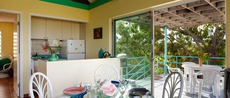 A dining area with a glass table, white chairs, and a view of a balcony with a railing.