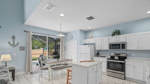 Une cuisine moderne avec des meubles blancs, un îlot central et un coin repas comprenant une table et des chaises.
