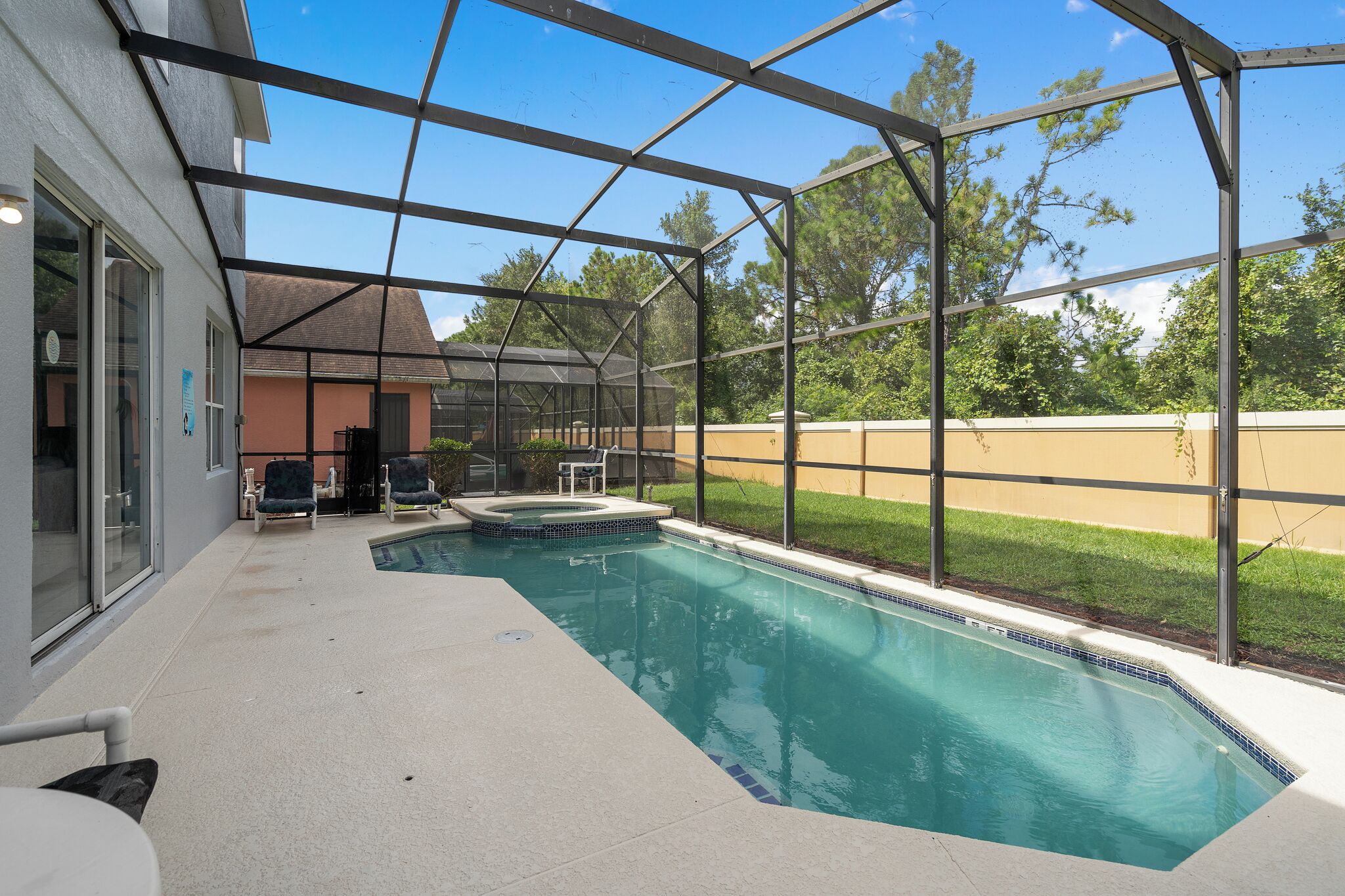 A covered outdoor swimming pool with a hot tub, surrounded by a house and a grassy area.