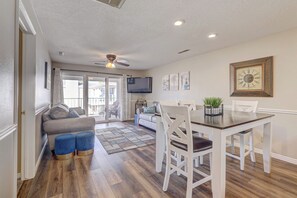 A dining area with a wooden table and white chairs, a gray sofa, and a TV mounted on the wall.
