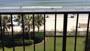 A balcony with a view of the beach, palm trees, and a sandy area with umbrellas. - Check This One Out! Best Location-Quiet And Nice Wide Beach-Direct Ocean Front (Myrtle Beach)