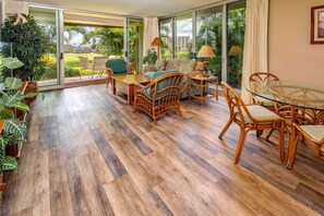 Ein geräumiges Zimmer mit einem großen Schiebeglastür, die zu einem Garten führt, mit Korbmöbeln und einem Glastisch.