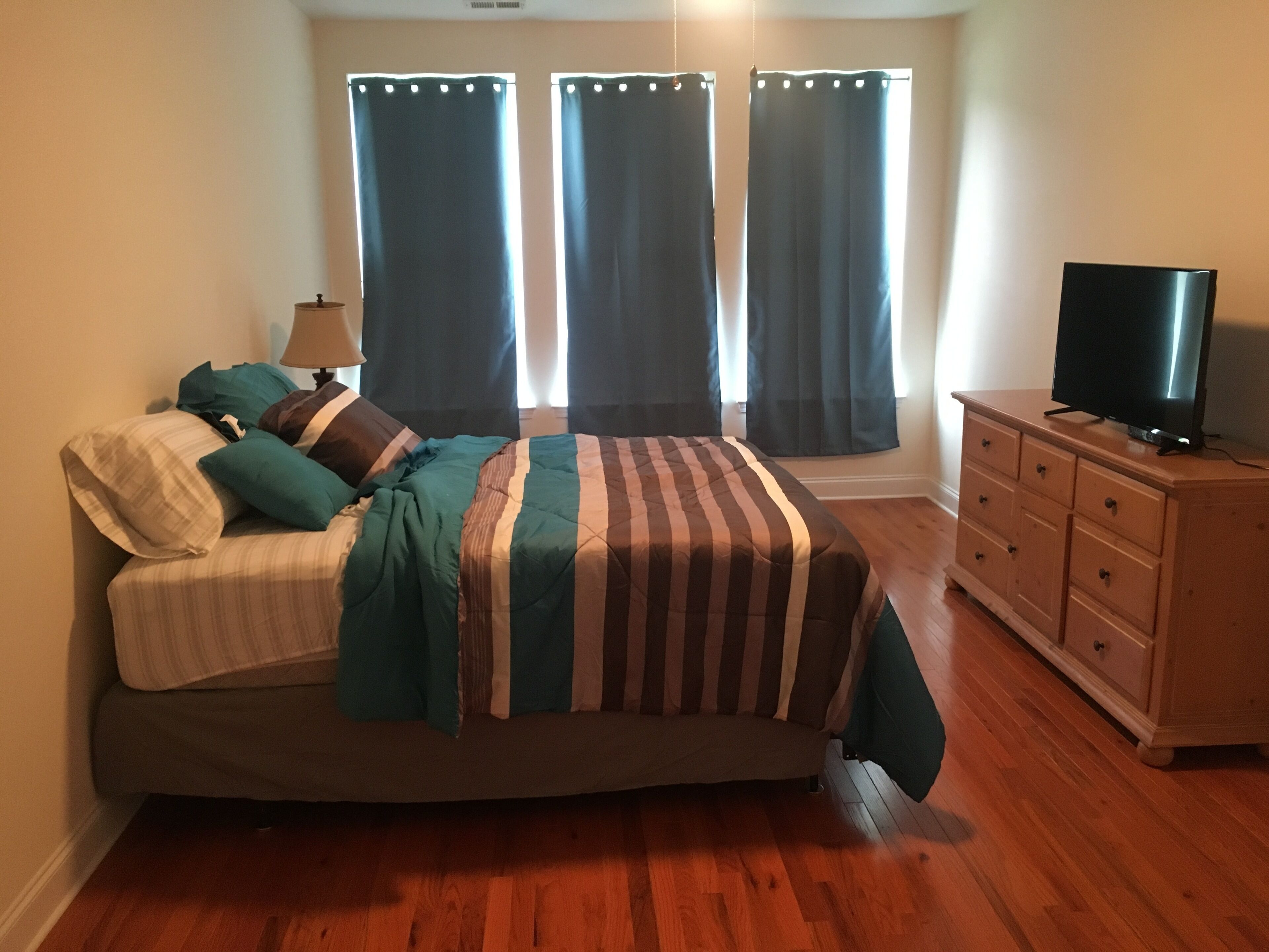 Un dormitorio con cama, cómoda, televisor y cortinas.