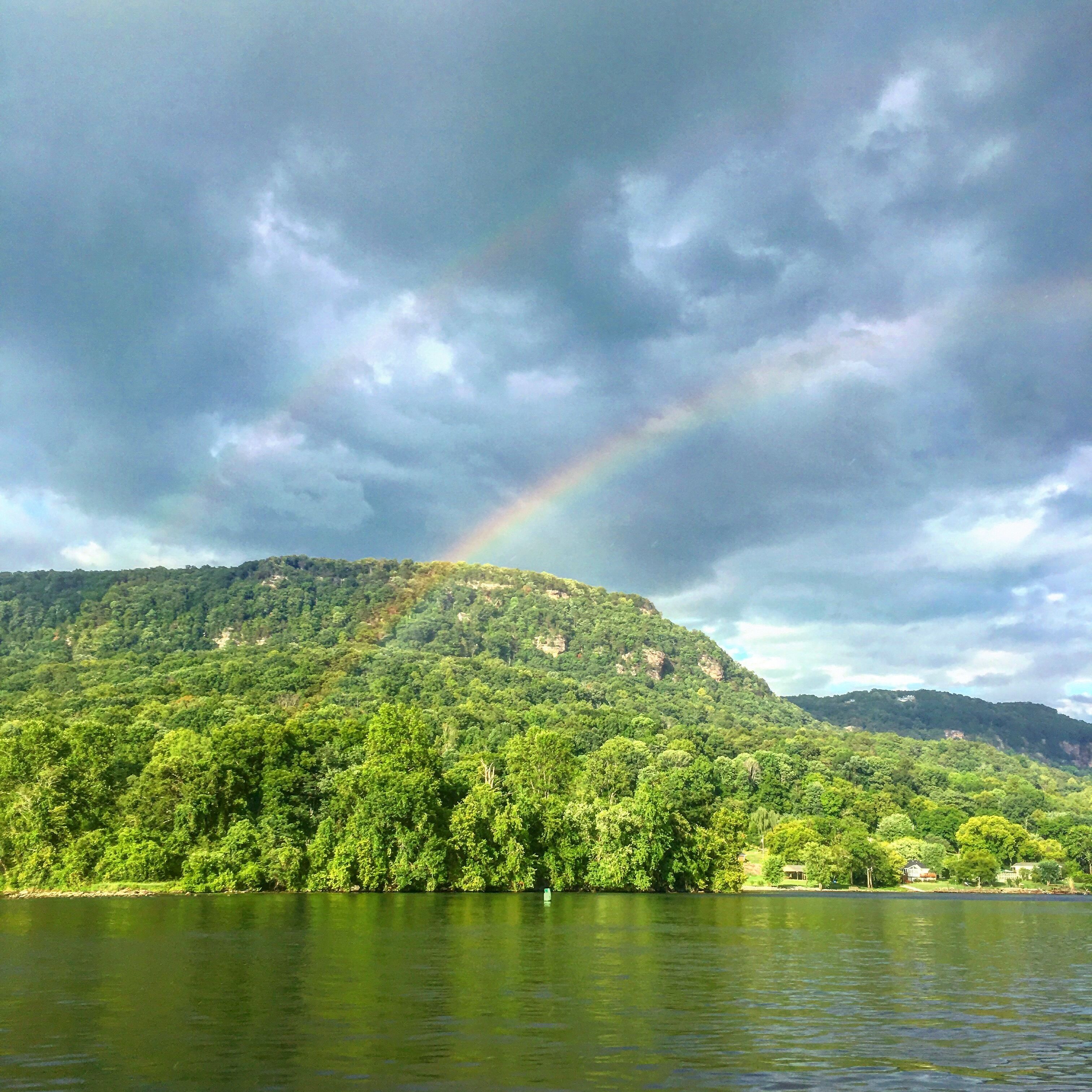 Een weelderig groen landschap met een berg, een meer en een regenboog.