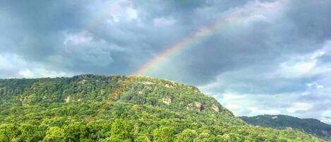 Een weelderig groen landschap met een berg, een meer en een regenboog.