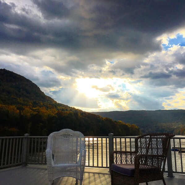 A balcony with wicker chairs overlooking a body of water and a forested hillside.