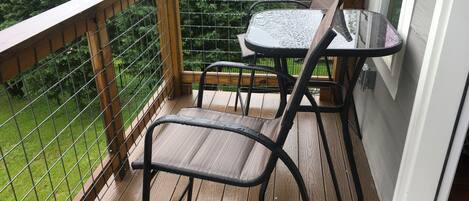 A wooden deck with a metal railing, two chairs, and a small table.