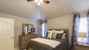 Een slaapkamer met een bed, dressoir, spiegel en plafondventilator.