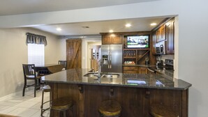 Een keuken met een groot eiland, houten kastjes, een roestvrijstalen koelkast en een televisie.