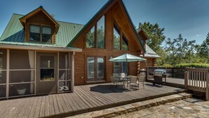 Eine Blockhütte mit einer Veranda, großen Fenstern und einem Grillplatz.