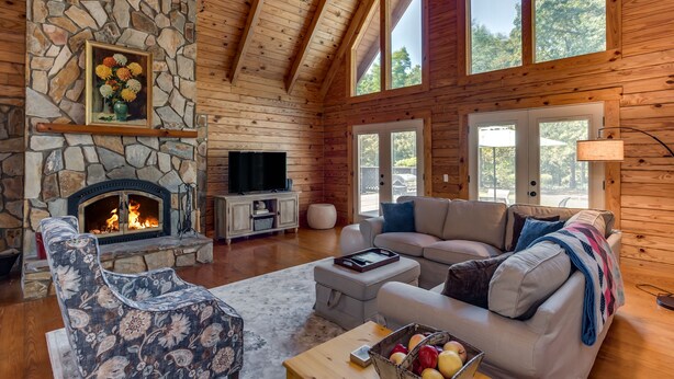 Ein rustikales Blockhaus-Interieur mit Kamin aus Stein, Holzbalkendecke, einer Couch und einem Fernseher.