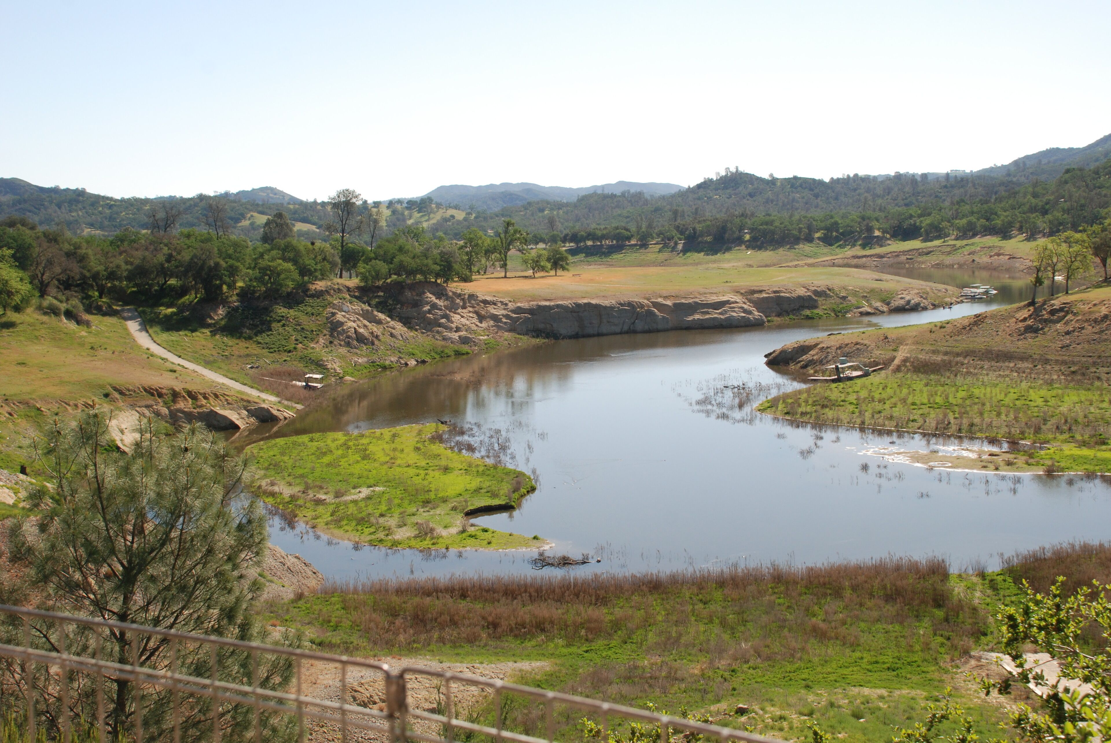 Un río serpentea por un paisaje montañoso con un sendero de tierra a su lado.