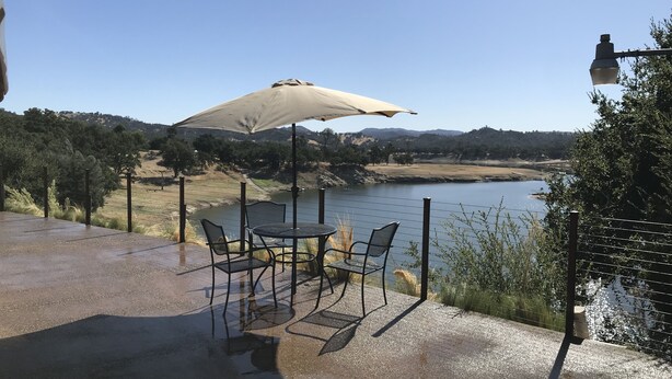 A patio with a table and chairs, overlooking a body of water and hills. - Lake front home private dock (Paso Robles)