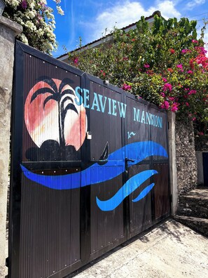 Una entrada cerrada con un mural de una puesta de sol, palmeras y un bote, identificada como "SEAVIEW MANSION".