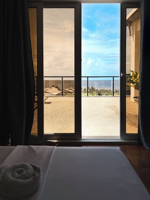 Una habitación con cama, vista a un balcón con barandilla y una puerta que da al exterior.