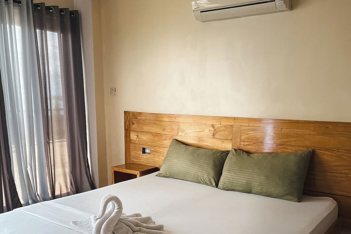 Cama bem arrumada com toalha, cabeceira de madeira e dois travesseiros.