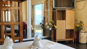 A hotel room with a bed, towels, a TV, a wooden chair, a small table, and a view of the sea. - Seaview Mansion (Dalaguete)