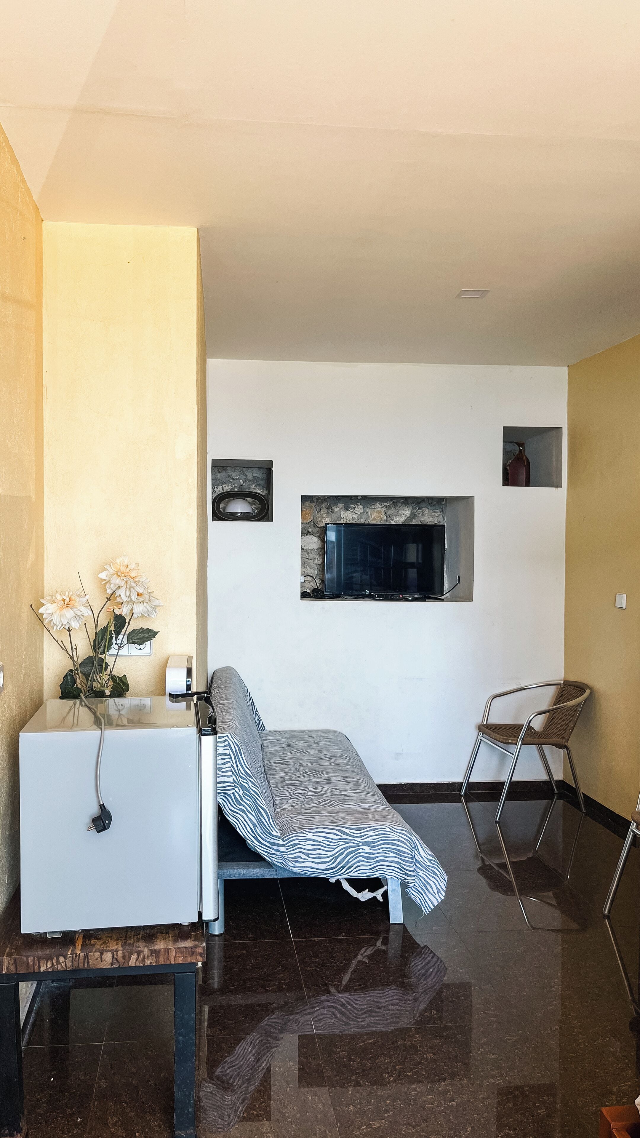 Una habitación pequeña con cama, escritorio, silla y televisor en la pared.