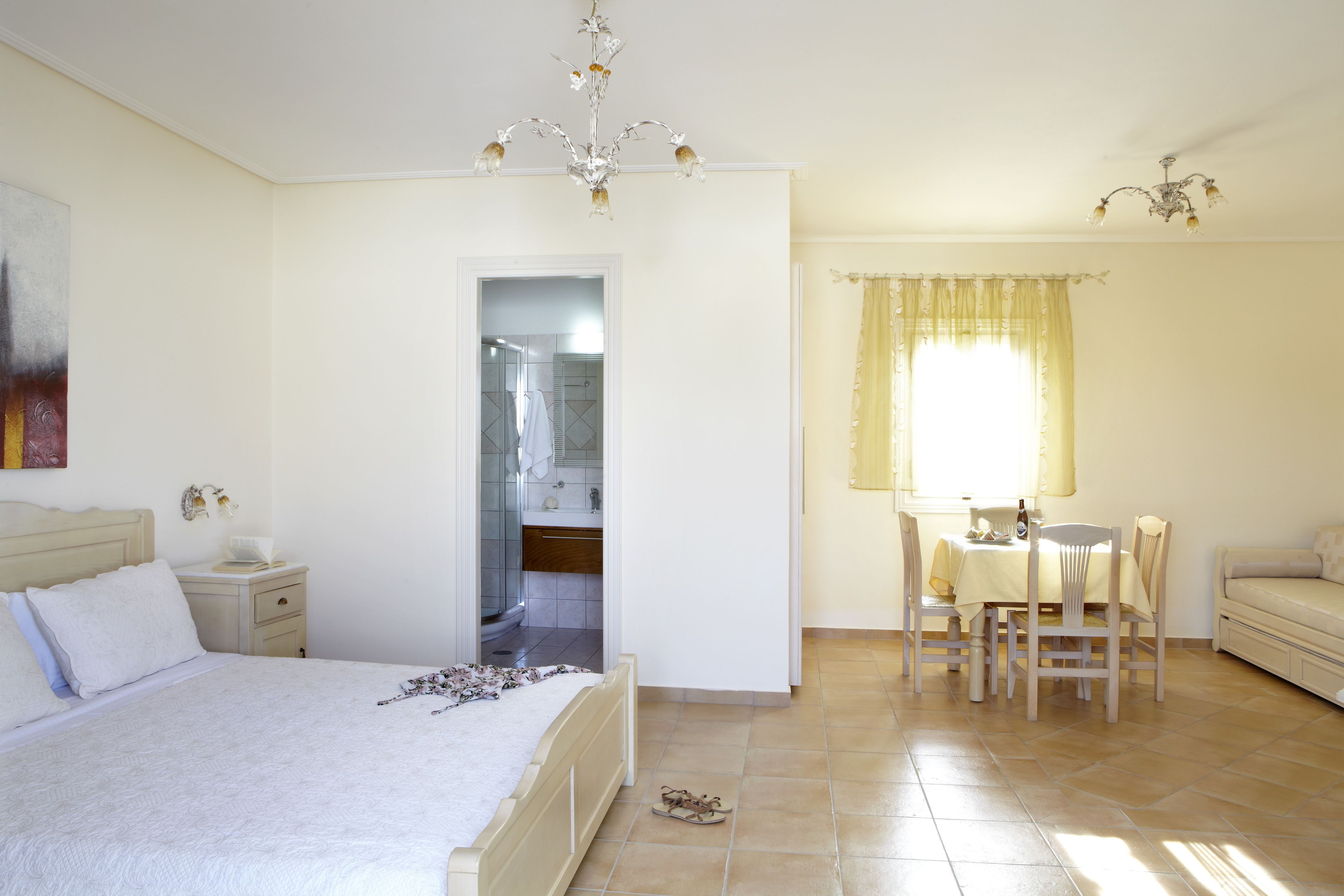 Camera da letto con un letto, comodino e un piccolo tavolo con sedie. Si intravede un bagno attraverso una porta aperta.