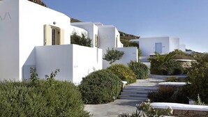 A row of white buildings with a staircase leading to a higher level, surrounded by greenery and a clear sky. - Hotel Mediterranean (Naxos)