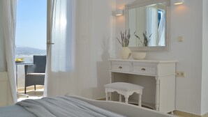 A bedroom with a bed, a white dresser with a mirror, and a view of the outdoors through a window. - Hotel Mediterranean (Naxos)