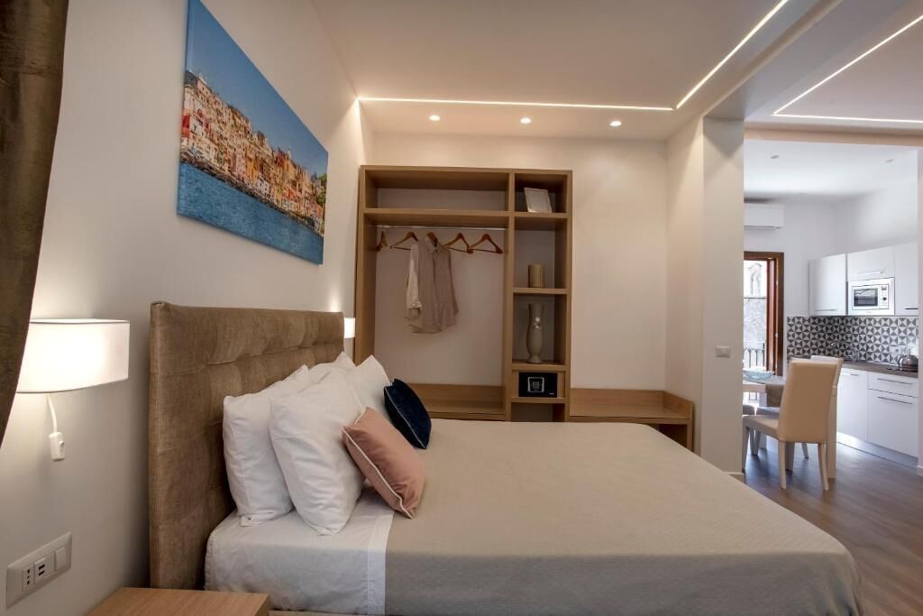 A modern hotel room with a large bed, a walk-in closet, and a view of the kitchen.