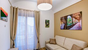 Un salon avec un canapé beige, un plancher en bois, une grande fenêtre avec des rideaux beiges et un tableau accroché au mur.