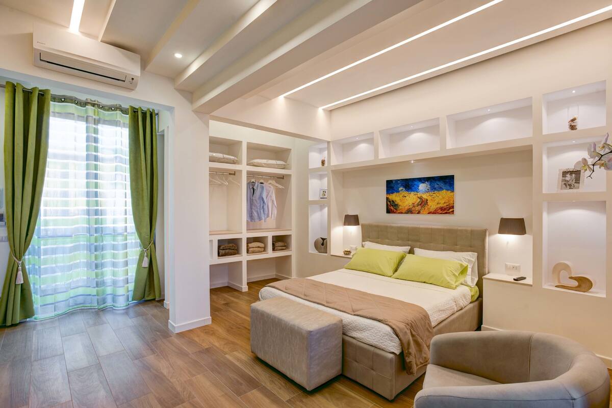 Een slaapkamer met een bed, bedlampen, een nachtkastje, een stoel, een kast en een schilderij aan de muur.