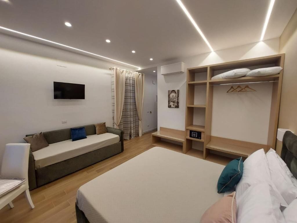 Une chambre d’hôtel moderne équipée d’un lit, d’un canapé, d’une télévision, d’une armoire et d’un petit bureau.