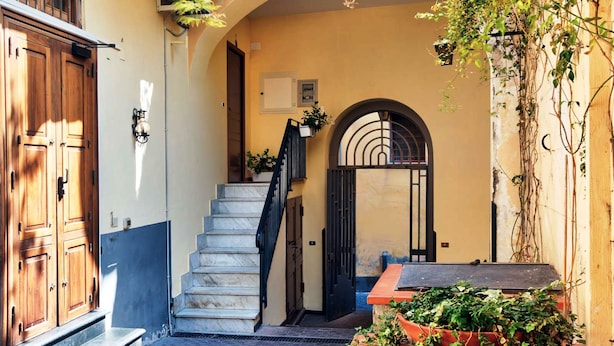 Une ruelle étroite avec un escalier en pierre menant à une porte, une porte en bois sur la gauche et un climatiseur fixé au mur.