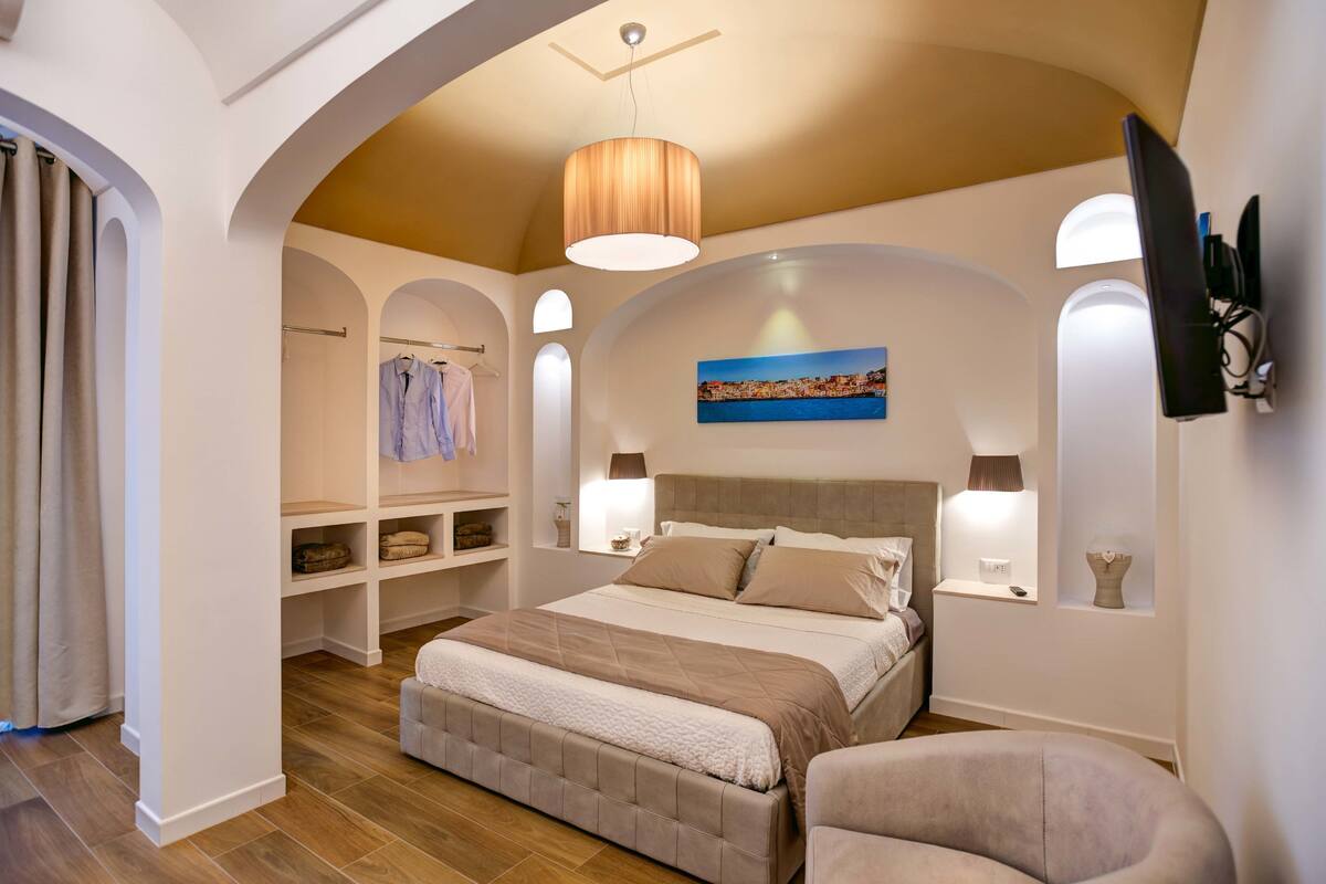 Een slaapkamer met een groot bed, inbouwkasten, een schilderij en een aan de muur bevestigde televisie.