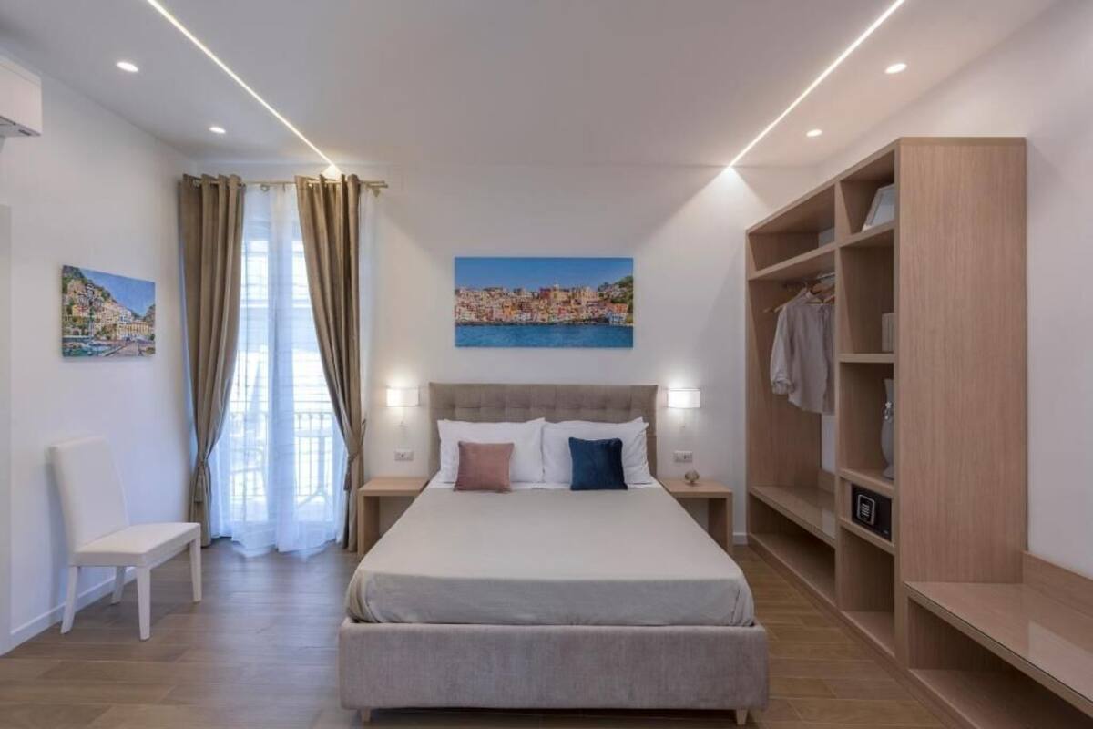 Een moderne slaapkamer met een groot bed, nachtkastjes, een garderobe en uitzicht op een kustplaats.